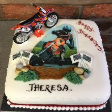 Personalised photo cake featuring a photo of a person on a motocross bike. The cake is square and white.