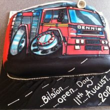 A personalised photo cake with a photo of a fire engine on the front. The cake is red and 3D icing details.