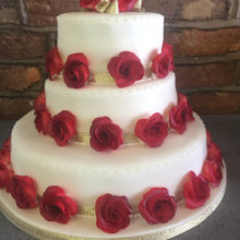 A three tiered wedding cake. The cake is white with red icing roses around every layer.