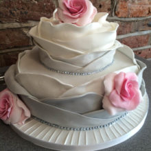 Two tiered wedding cake resembling a rose. The cake is grey with pink roses. Cake on display at a cake shop in Wolverhampton.