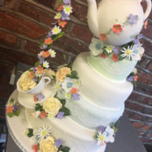 4 Tiered wedding cake with a icing teapot on top. The cake also has a icing teacup and flowers.