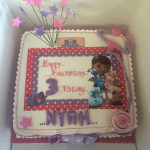 A personalised photo cake for a three year old child. The cake has character photos and is pink and purple.