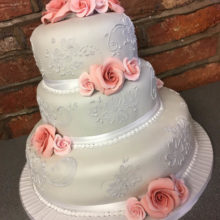 Three tier wedding cake with pink icing roses. The cake is on display in a cake shop in Wolverhampton.