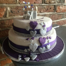 Two tiered wedding cake with purple and silver icing hearts.