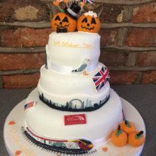 A white 3 tiered wedding cake with pumpkin bride and groom toppers. The cake is on display in a cake shop in Wolverhampton.