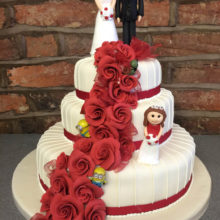 A three tiered wedding cake. The cake is white with red roses. The cake is on display in a cake shop in Wolverhampton.