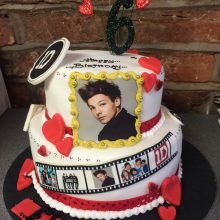 A personalised photo cake featuring a photo of One Direction. The cake is two tired, white with icing hearts.