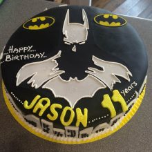 A personalised photo cake with a photo of Batman on the front. The cake is circular in shape and black in colour.