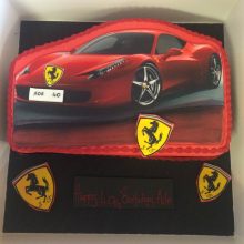 A personalised photo cake red in colour with a photo of a Ferrari on the front.