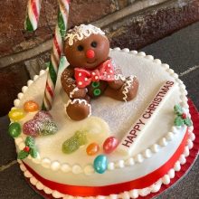 A bespoke cake, round and white in colour. The cake has jelly beans on top and a ginger bread man made out of icing.