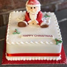 A bespoke cake, square in shape with a Santa figure sat on top made out of icing sugar.