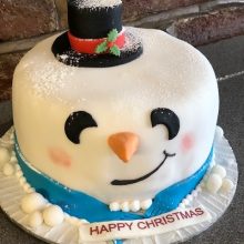 A bespoke cake made to look like a snowman's head. The cake has been dusted with icing sugar to look like snow.