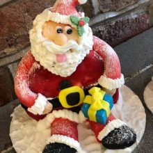 A bespoke cake crafted to look like Santa sitting in the snow holding a gift.