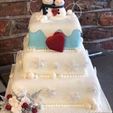 A bespoke three layered cake. The cake is white with two snowmen on the top.